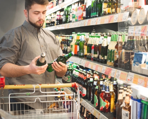 Man with a beard stands in a supermarket in an alcoholic department and holds two bottles with beer in his hands